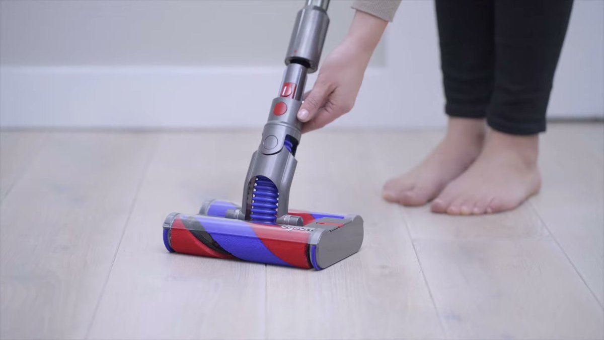 Person using Dyson Omni-Glide on hardwood floor, showing handle and brush head
