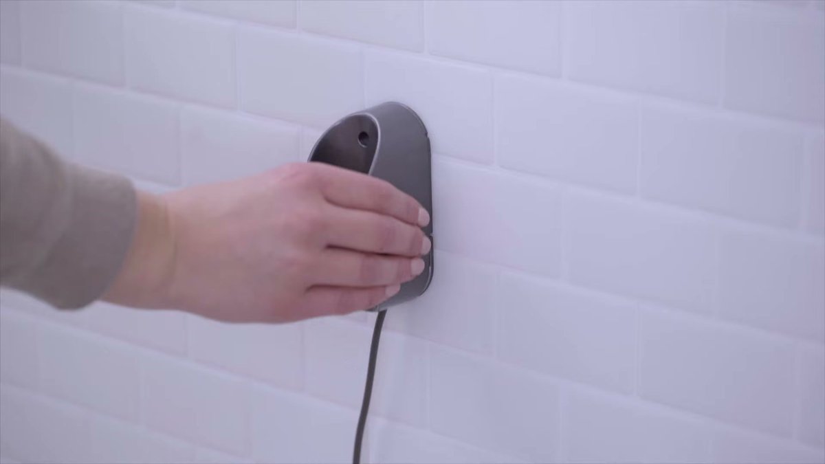 Hand docking Dyson Omni-Glide on wall-mounted charging base in white tiled kitchen