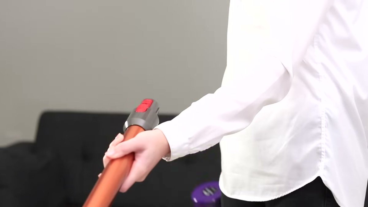 Person using Dyson V10 Absolute cordless vacuum in a living room setting