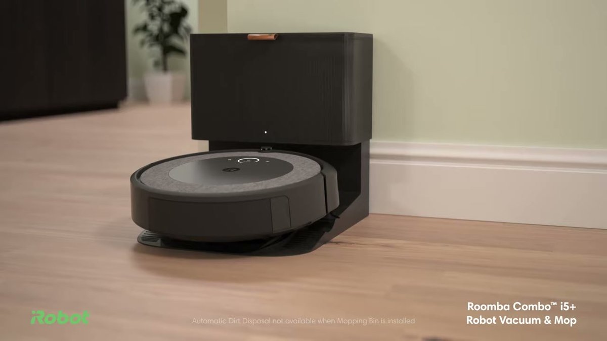 iRobot Roomba i5+ docked at its charging base on hardwood floor in a living room setting